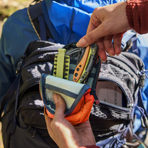 Translation missing: en.Person retrieving a Leatherman Skeletool® CX in Aurora color out of a Leatherman Tool Pouch in Aurora color, showcasing a mojito colored bit kit in an outdoor setting