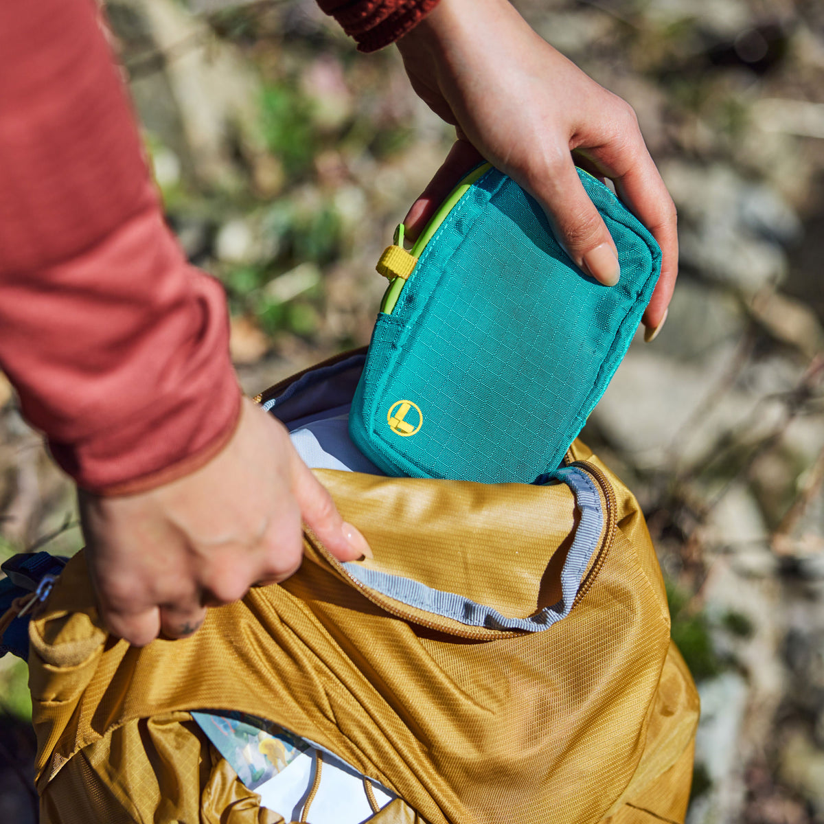 Translation missing: en.Person placing a Teal Twist Leatherman tool pouch into the open top of a mustard-yellow backpack outdoors