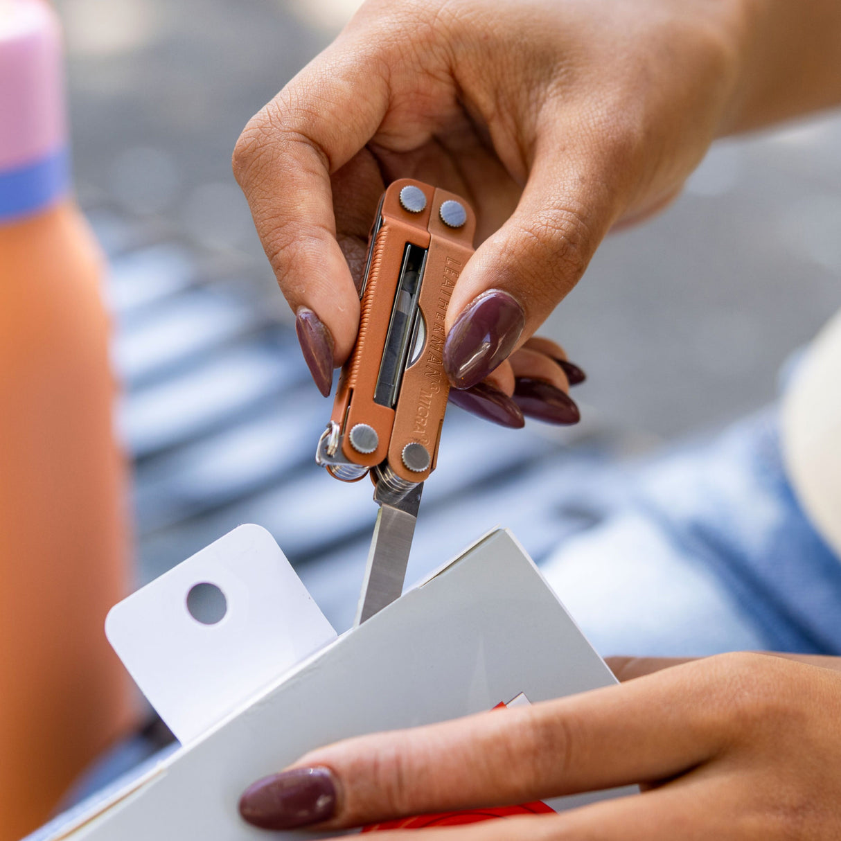 Translation missing: en.Close-up of a hand using the knife on a Pumpkin Spice Leatherman Micra® multi-tool to cut open packaging