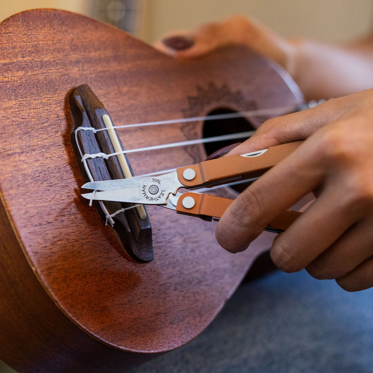 Translation missing: en.A hand using the scissors on a Pumpkin Spice Leatherman Micra® multi-tool to trim string ends on a wooden ukulele