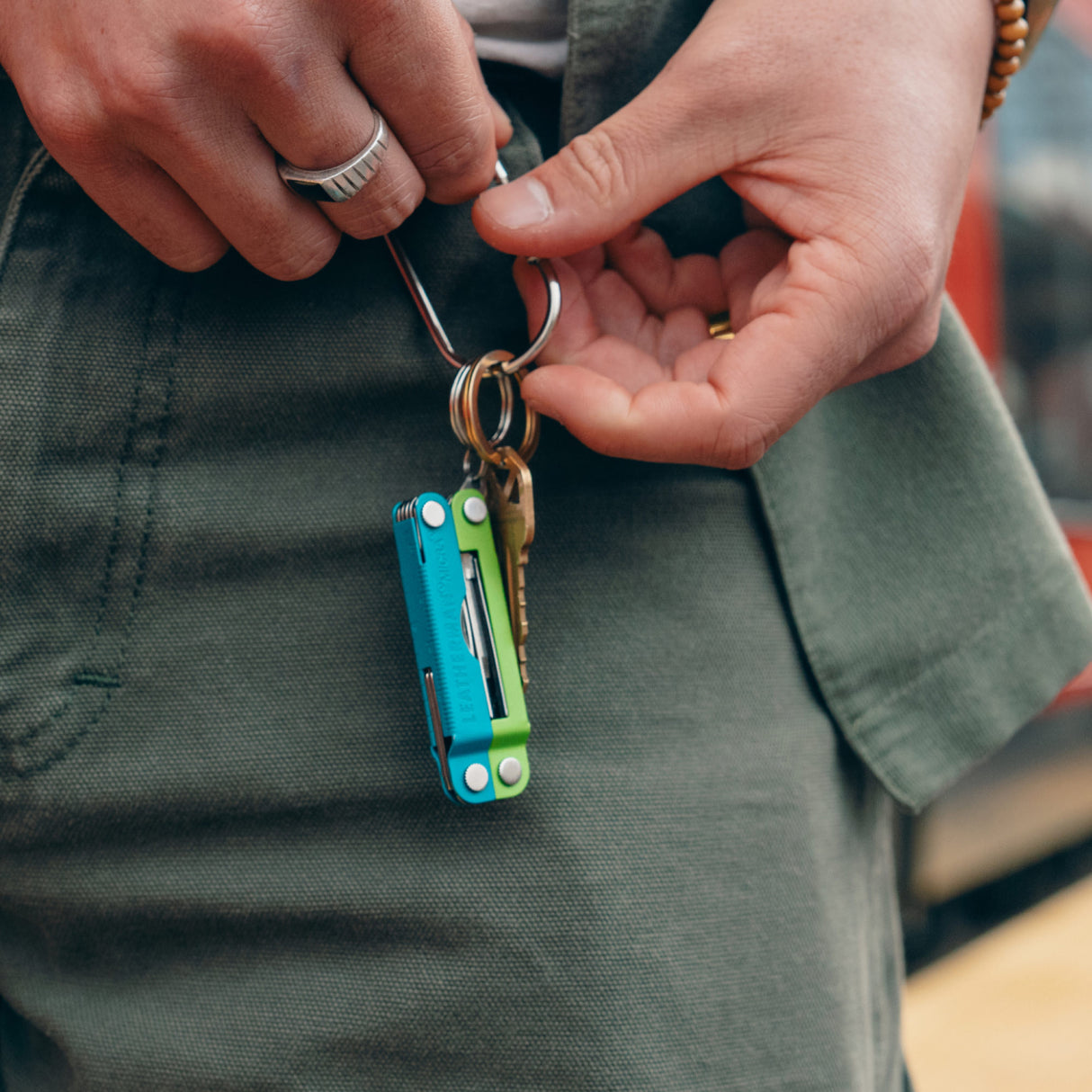 Translation missing: en.Person holding a keychain near a belt loop with a Leatherman Micra® in Teal Twist color on it, showcasing its compact design