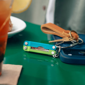 Translation missing: en.Leatherman Micra® in Teal Twist color attached to a keychain resting near a phone, showcasing its compact size