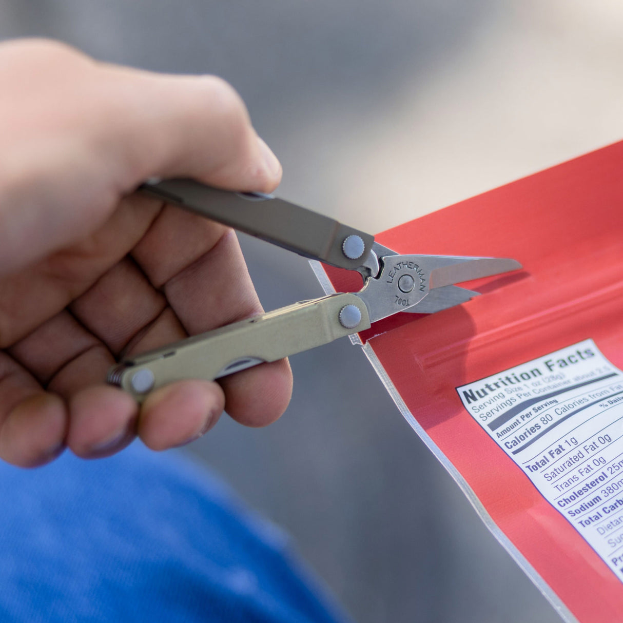Translation missing: en.Person using the scissors on a Winter Fog Leatherman Micra® to cut open red snack package