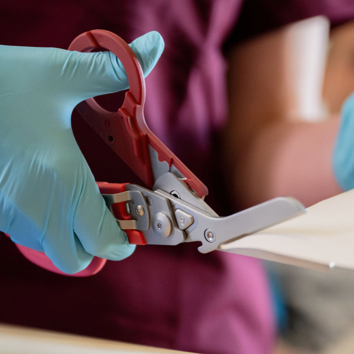 Translation missing: en.A nurse wearing blue gloves using the shears on a Raspberry Rose Leatherman Raptor® Rescue to cut gauze