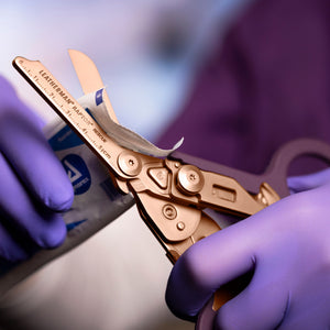 Translation missing: en.Rose Gold Raptor® Rescue shears cutting open medical packaging held by gloved hands