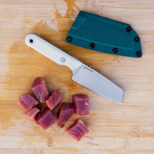 Translation missing: en.A Leatherman Rustle Alpine knife on a wooden cutting board next to a teal sheath and freshly cut chunks of raw fish