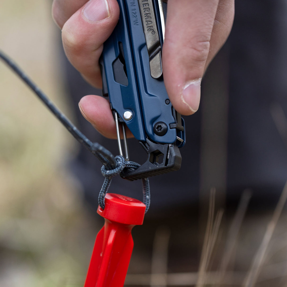 Translation missing: en.A person using the carabiner on a Nocturnal Leatherman Signal® to attach to a rope on a tent stake