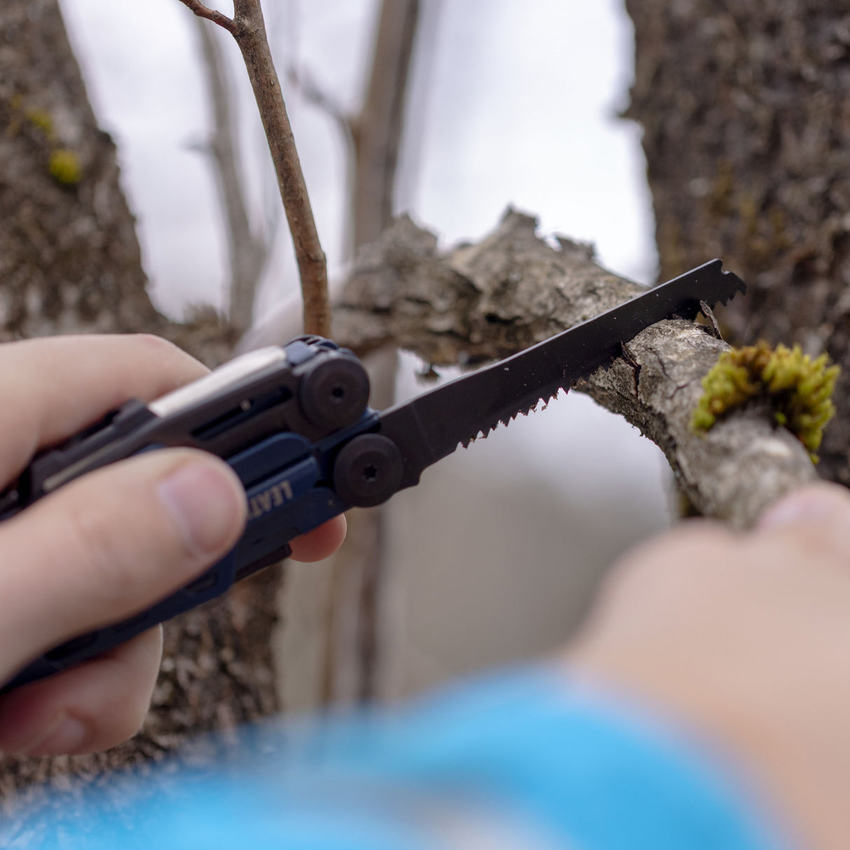 Translation missing: en.A person using the saw on a Nocturnal Leatherman Signal® to cut a branch