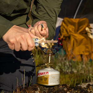 Translation missing: en.Hands using a Sandstorm Signal multitool to strike sparks onto a small camping stove outdoors