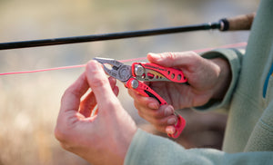 Translation missing: en.Hands using a Guava Skeletool® CX multitool pliers to grip a bright fishing line outdoors