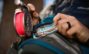 Translation missing: en.Person retrieving a Verdant Skeletool CX multitool from a zippered pack while holding a fishing reel