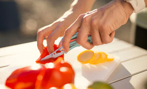 Translation missing: en.Hands using a Paradise Skeletool CX knife to slice red pepper and yellow squash on a cutting board