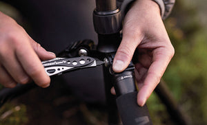 Translation missing: en.Hands using a Black &amp; Stainless Skeletool® CX to tighten a bolt on a tripod outdoors