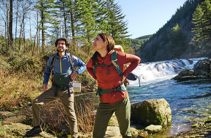Translation missing: en.Two hikers enjoying nature near a waterfall, showcasing outdoor adventure with the Aurora Skeletool® Cx