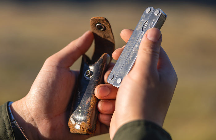 Translation missing: en.Person holding a Leatherman PST 2 in one hand and its worn leather case in the other, outdoors in natural lighting