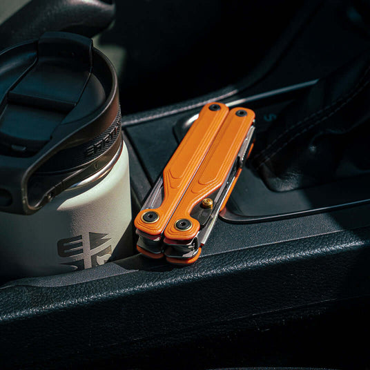 Translation missing: en.Orange Leatherman Wave® Alpha multitool resting beside a coffee cup in a car's center console
