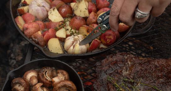 Leatherman Skeletool® poking garlic and potatoes in a camp fire skillet meal.