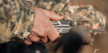 Hunting using a Leatherman Signal multi-tool to saw through a stick.