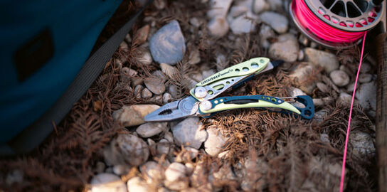 Opened Leatherman Skeletool<sup>®</sup>CX near backpack and fishing line reel. 