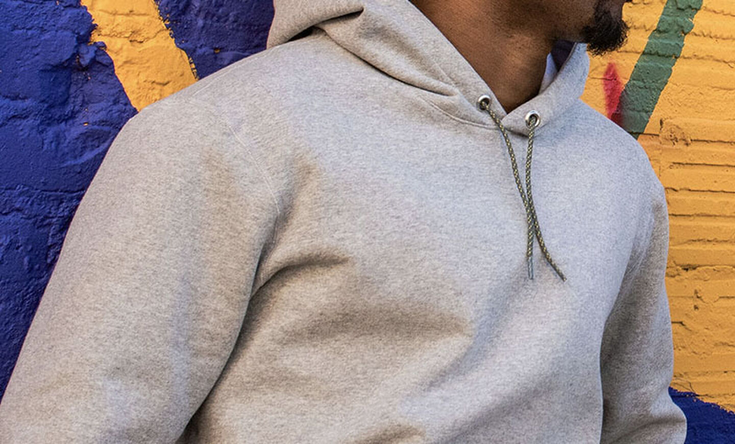 Man wearing Leatherman Basics Pullover Hoodie in gray stands against a mural wall.