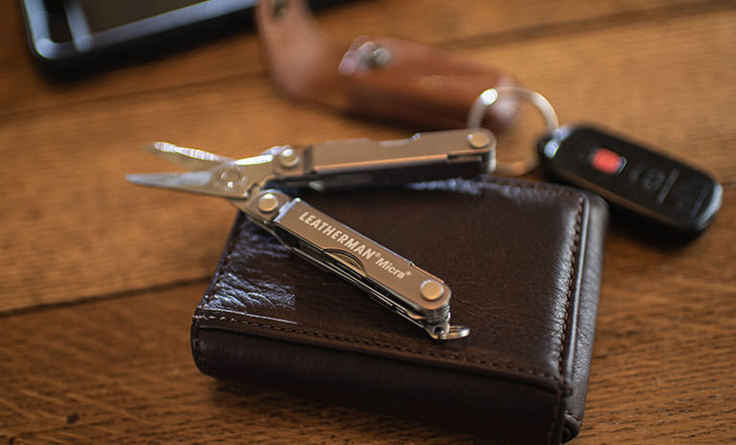 Stainless steel Leatherman Micra on top of dark brown wallet next to key fob on table 
