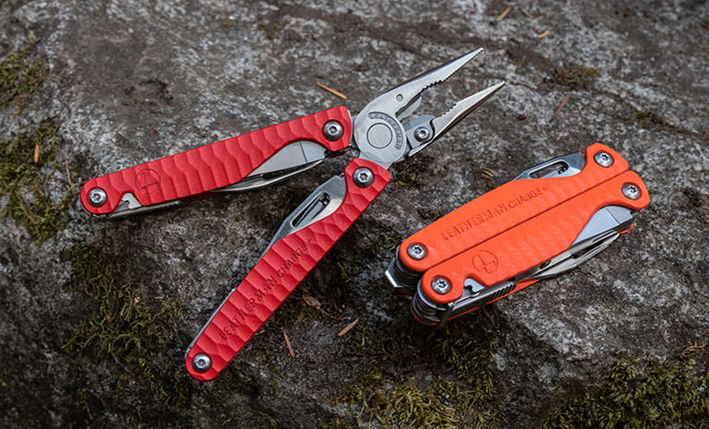 An open red Leatherman Charge+ G10 multi-tool laying on a rock next to a closed orange Leatherman Charge+ G10 multi-tool