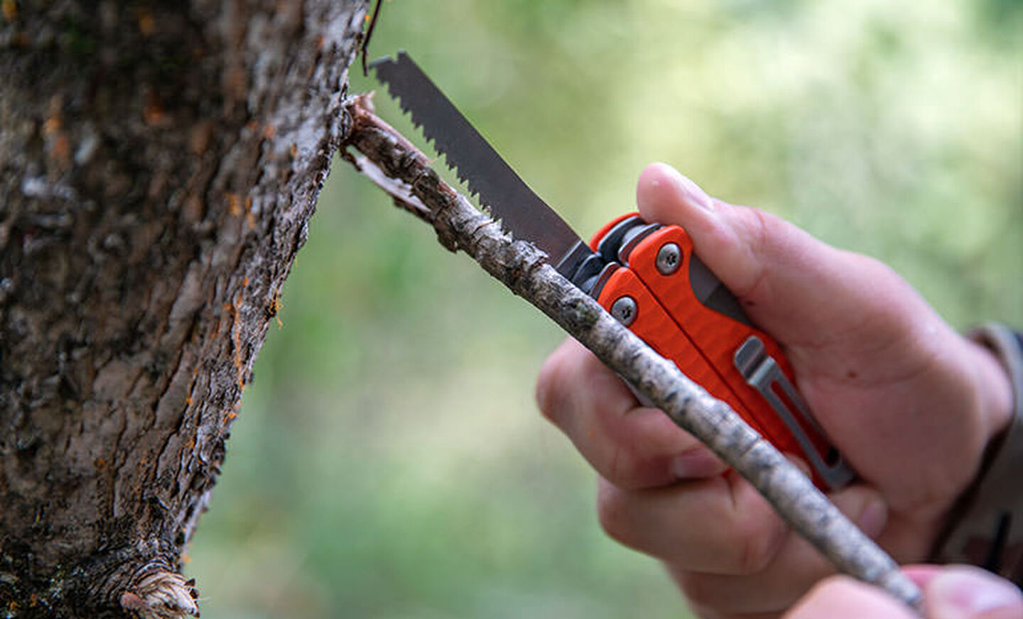 A person using the saw on an orange Leatherman Charge+ G10 to cut a branch