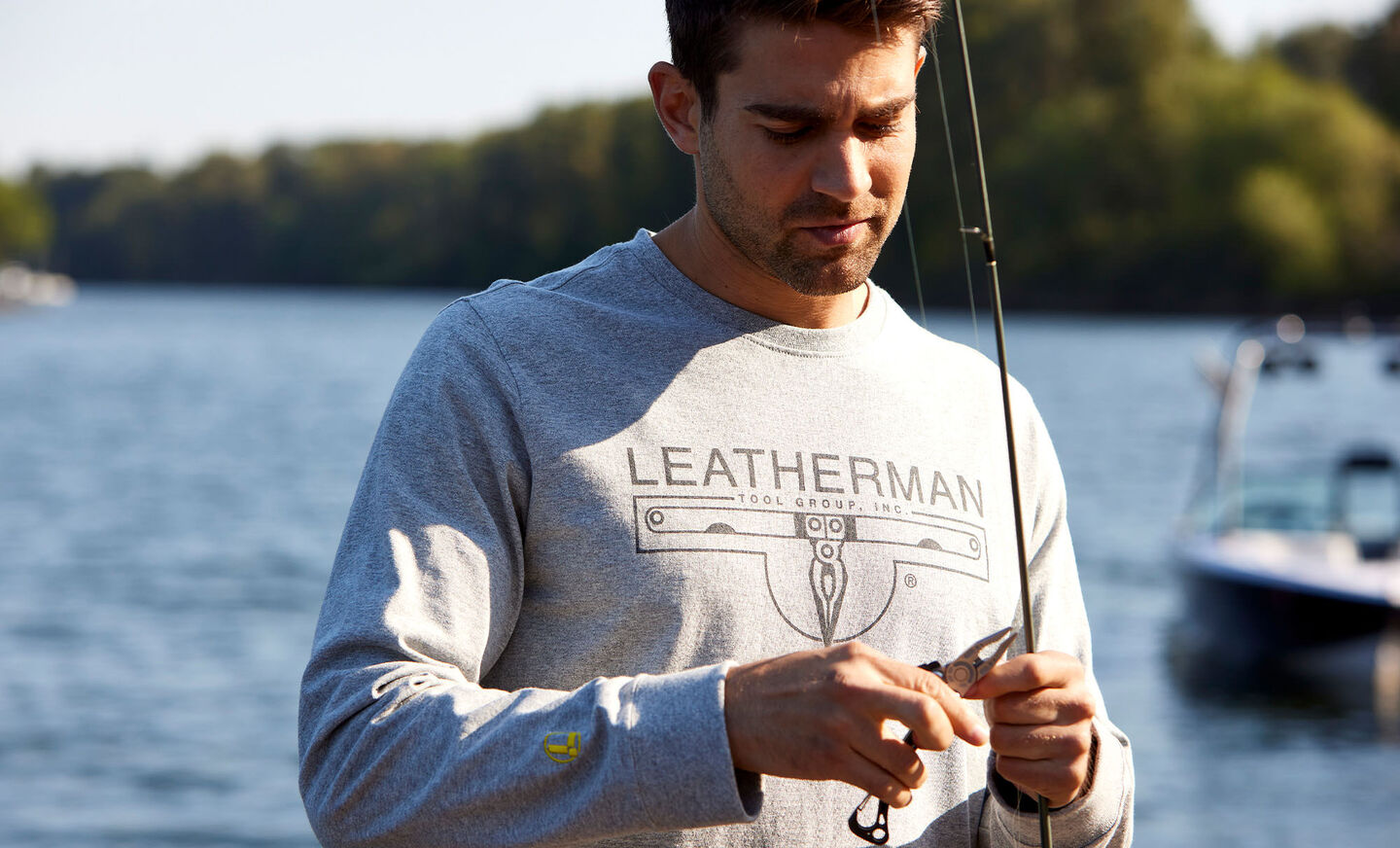 Man wearing gray Leatherman long sleeve logo t shirt by river using Leatherman tool to cut fishing line from rod