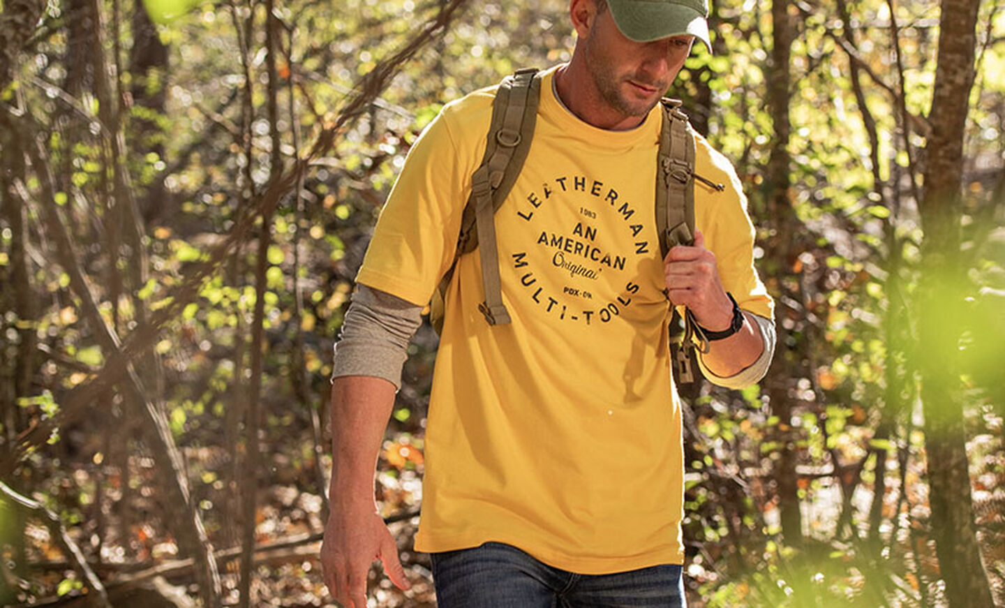 Man hiking through forest wearing Leatherman Heritage Badge Tee in yellow.