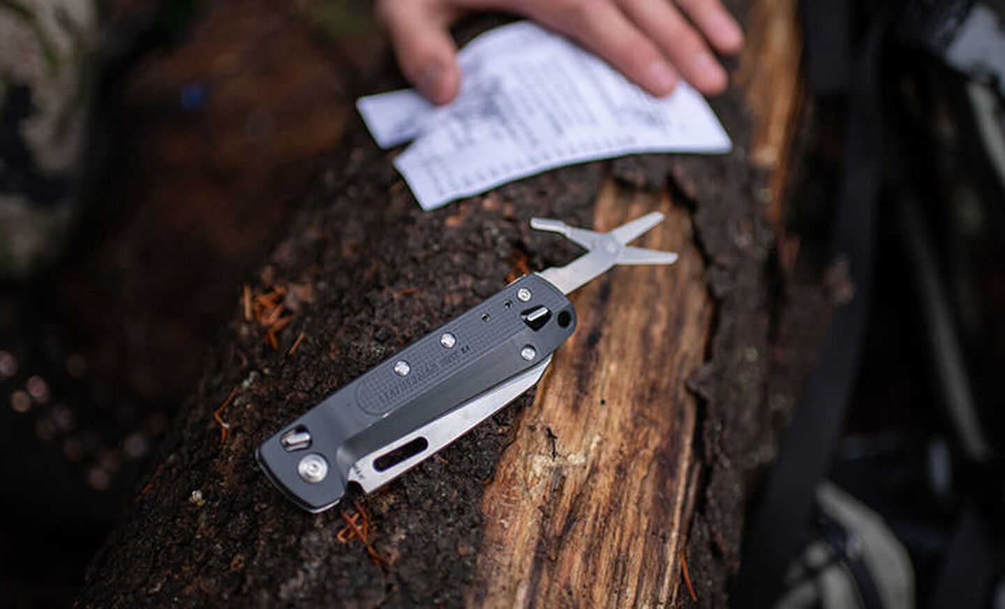 Man holding note next to Leatherman K4 with scissors opened on top of tree. 