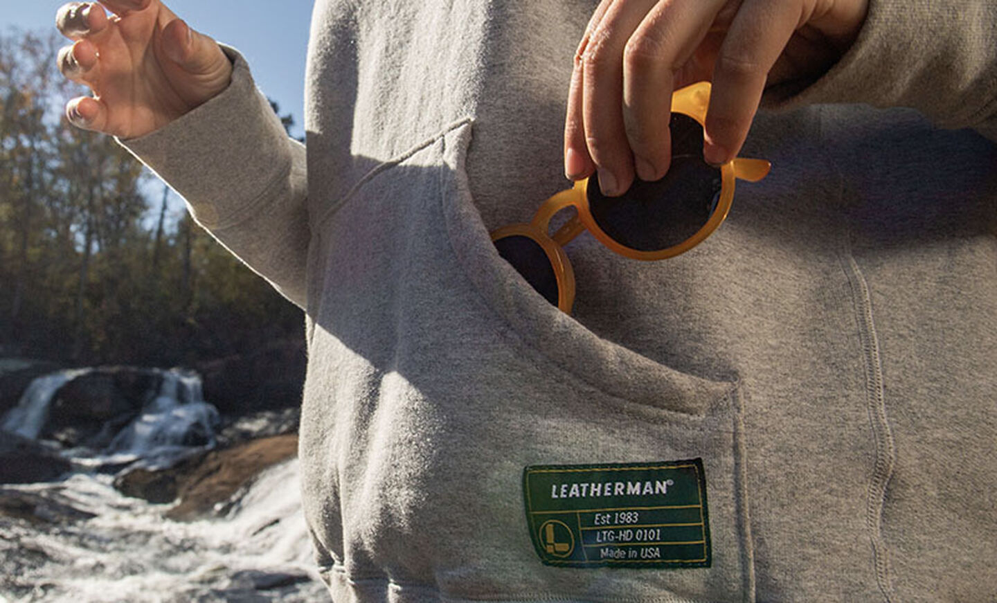 Sashing sunglasses in the front pouch of the Leatherman Basics Pullover Hoodie in gray.