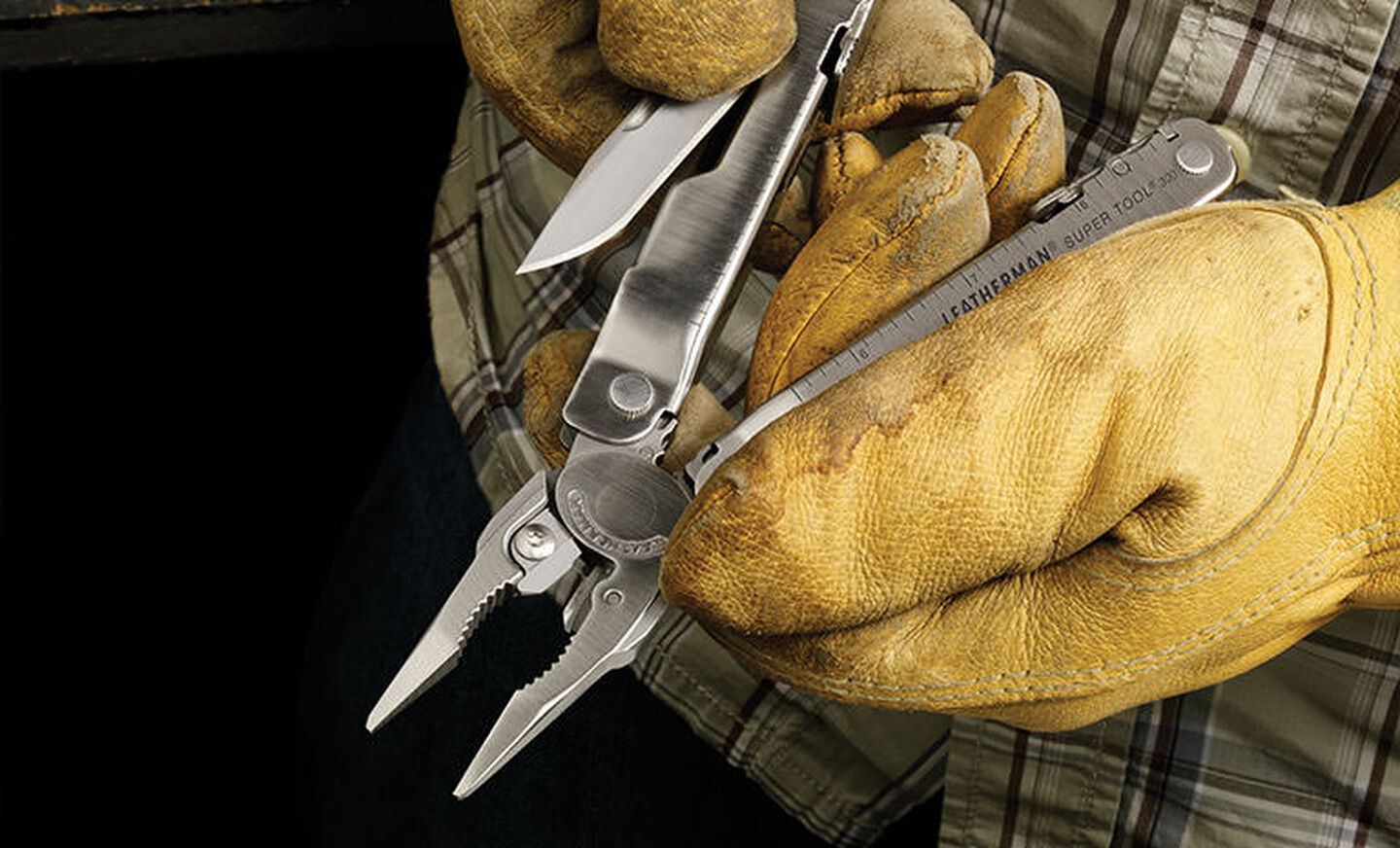 Man in green plaid shirt and yellow leather gloves pulling knife blade out of Leatherman Super Tool 300