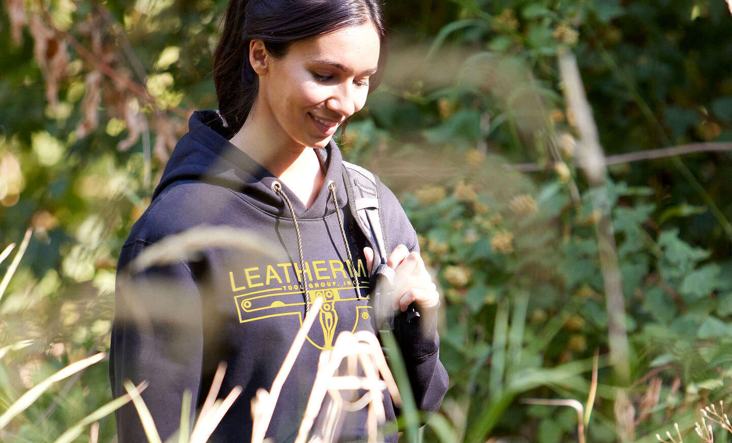 Woman wearing black Leatherman hoodie and yellow logo walking in woods 