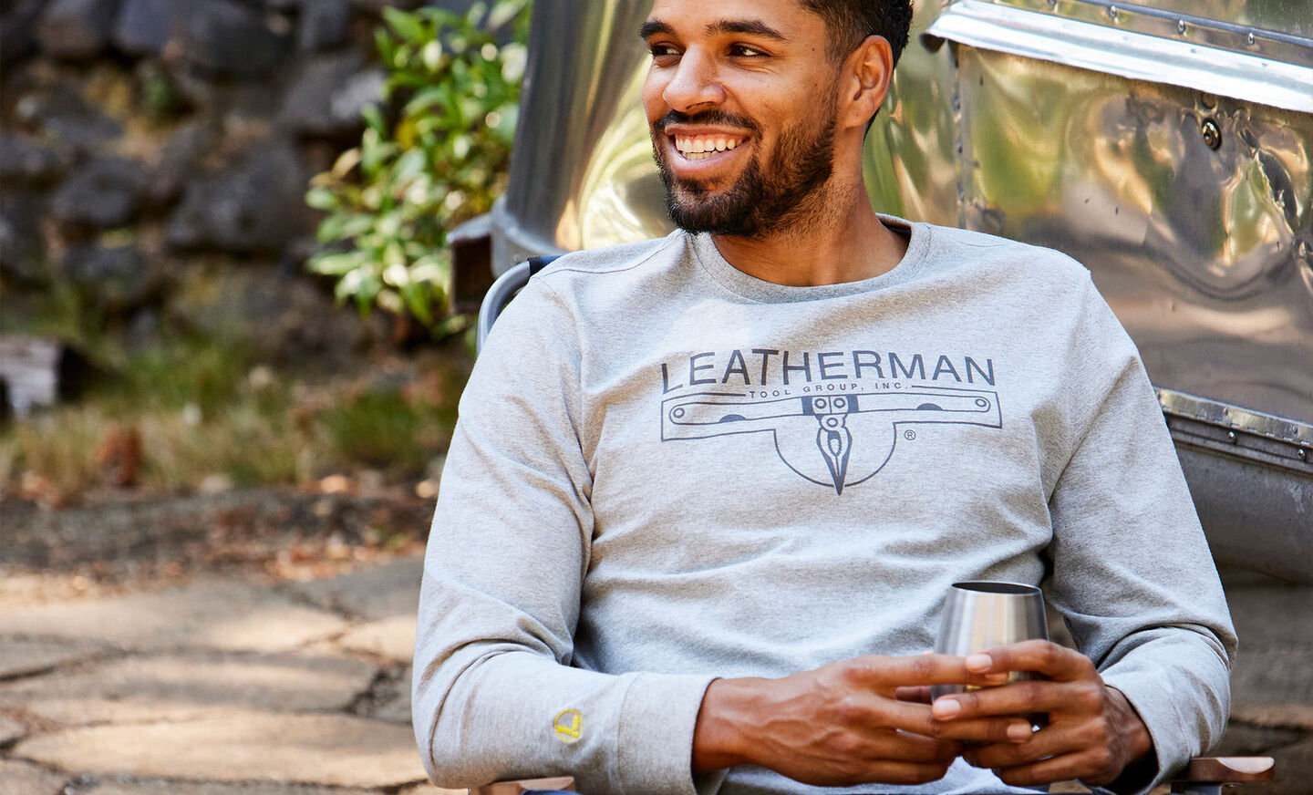 Man at camp wearing Leatherman long sleeve logo t shirt holding cup of coffee 