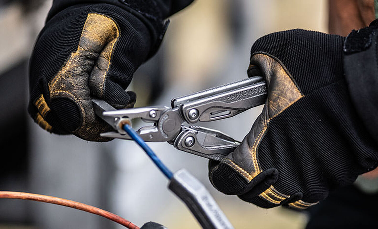 Man with dirty black and yellow safety gloves using Leatherman Charge+ TTI to crimp wire 