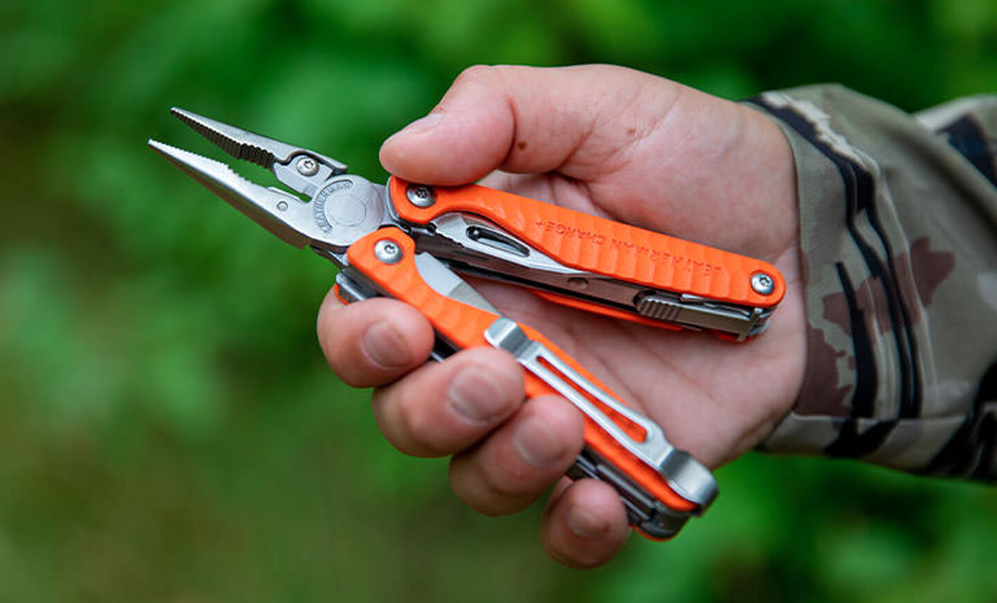 A person with an orange Leatherman Charge+ G10 in hand with the pliers open.