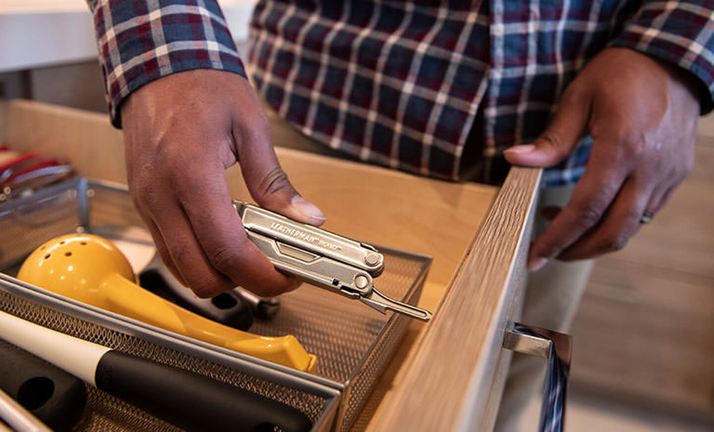 Man in red, white and blue plaid shirt holding Leatherman bond by kitchen drawer