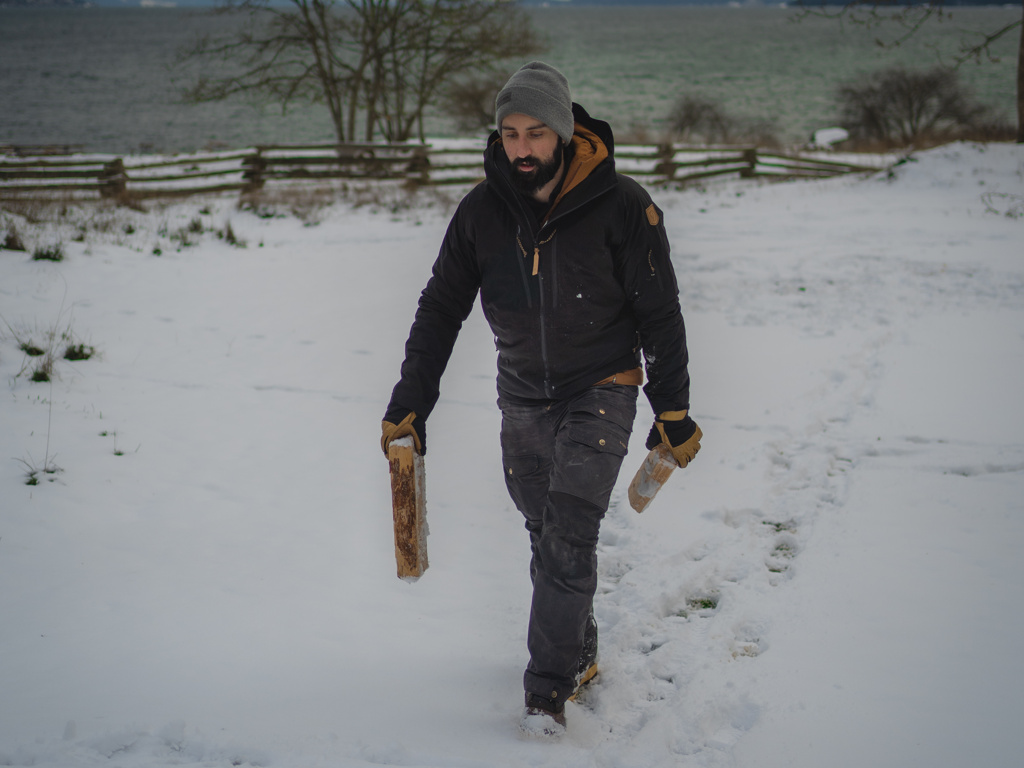 man walking in the snow with logs