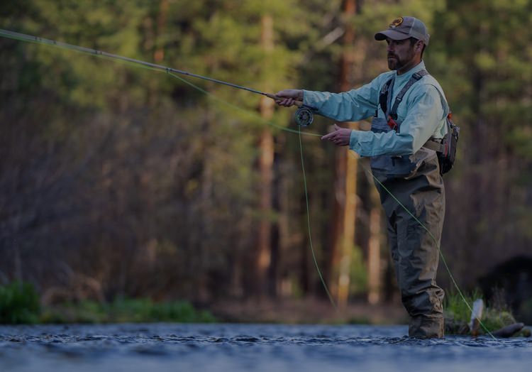  Uomo pesca con la mosca in un ruscello d'acqua dolce in un bosco.