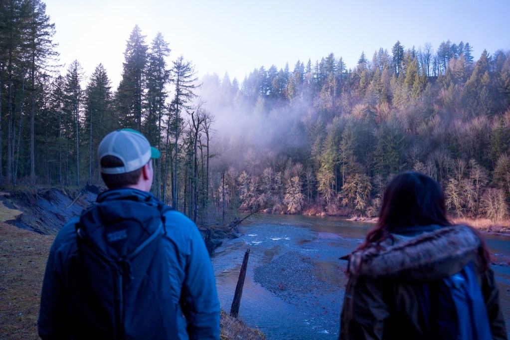 Two hikers taking in the view of a foggy Sandy river in Oregon.
