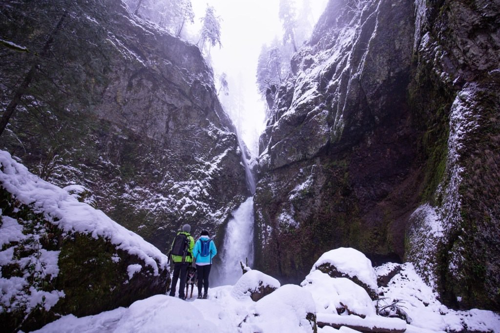 Two hikers taking in the beautiful scenery of a snowy Wahclella waterfall in Oregon.