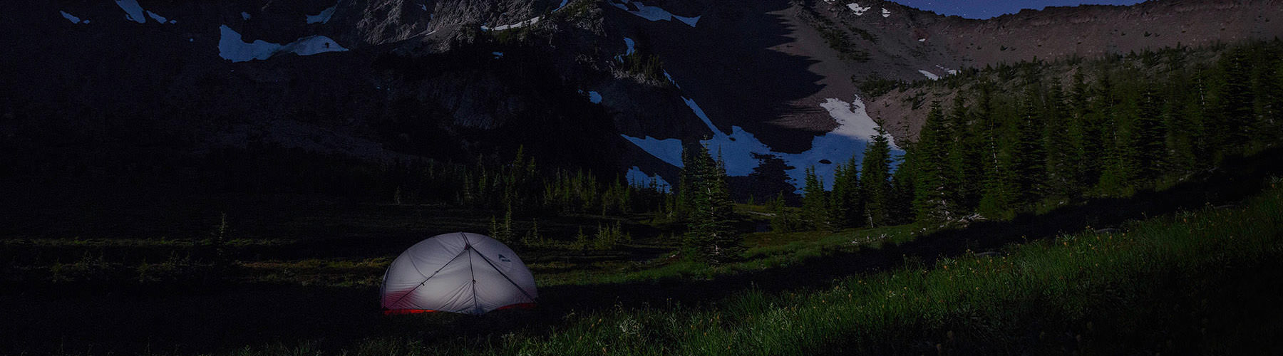 Camping tent pitched high in the snow capped mountains at night with stars twinkling in the skies.
