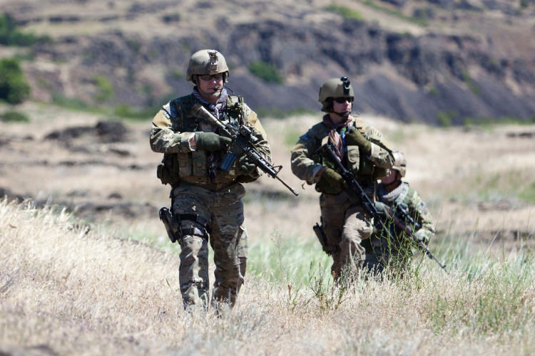 Military personnel hiking in formation across a field.