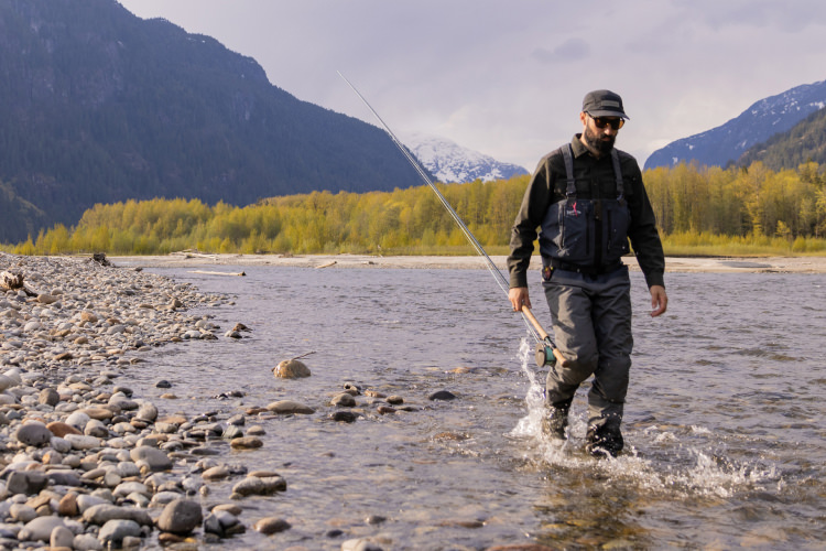 Fisherman walking on rocky river with fishing rod.