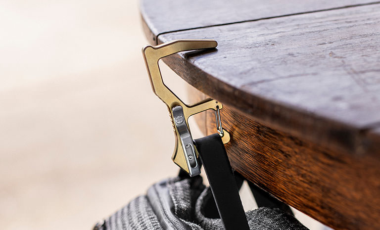 Brass Clean Contact Carabiner hanging a bag off a wooden table