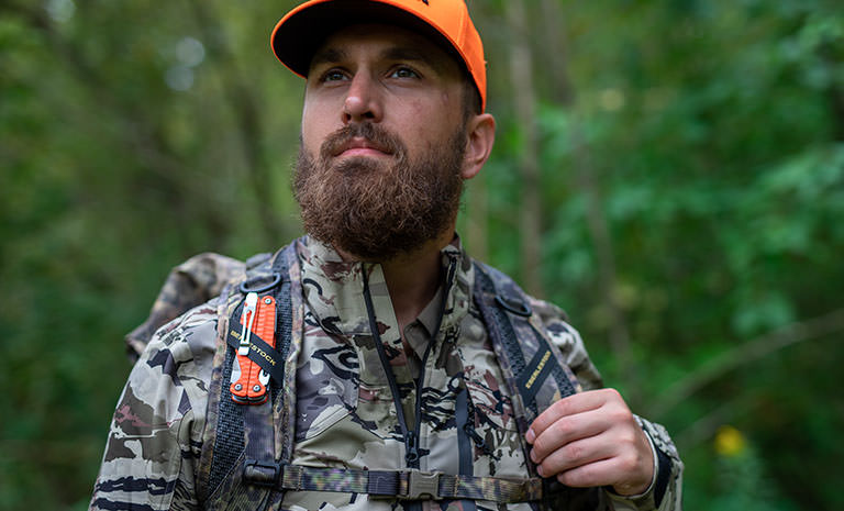 A hunter with an orange Leatherman Charge+ G10 multi-tool strapped to his backpack